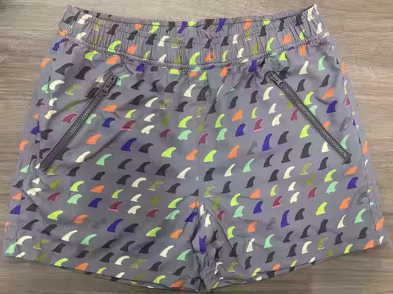 Front view of gray swim shorts with multicolor fin print and angled zipper pockets